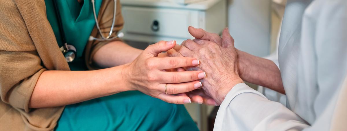 Close up of doctor comforting, holding senior patient's hand 