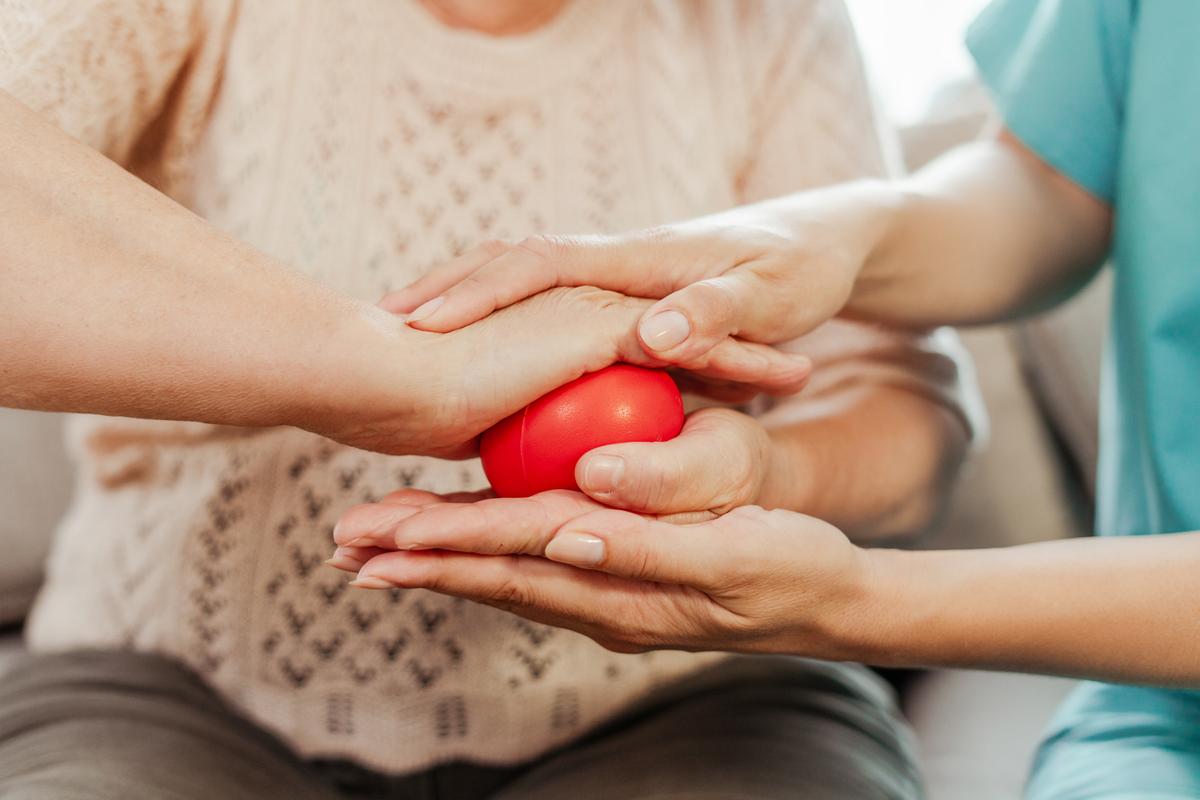 A nurse is assisting a sernior who is working with a red stress ball in their hands.