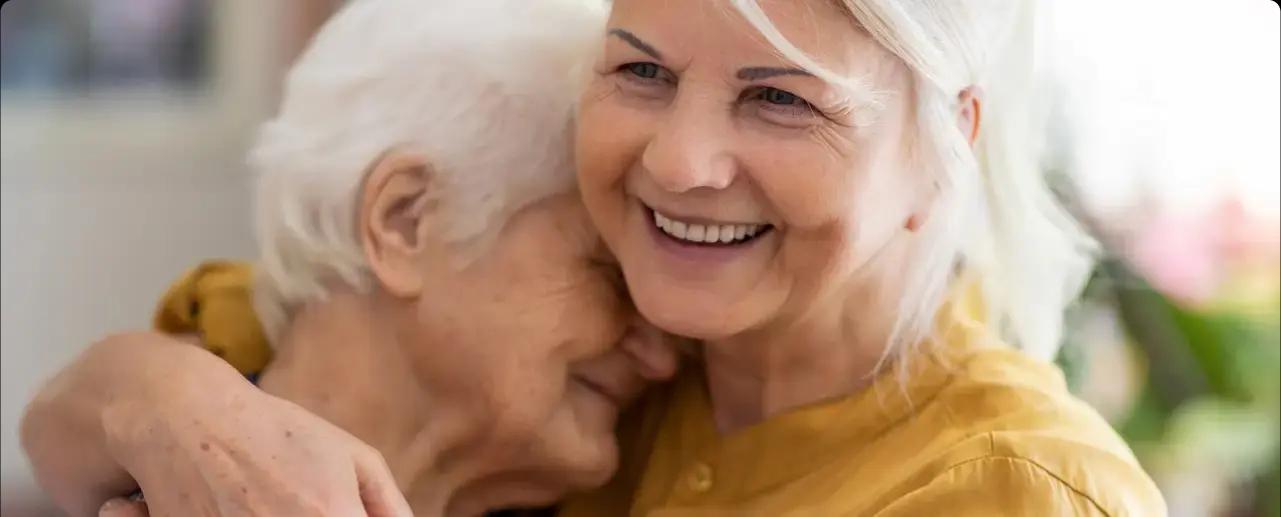 A senior mother and her daughter embrace with smiles